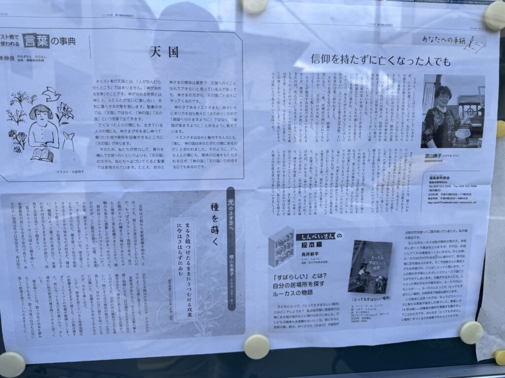 屋外の掲示板に貼られた教会関係のニュースレターの写真です。白い紙に黒い文字で複数の記事が印刷されており、上部には「天国」「信仰を持たずに亡くなった人でも」といった見出しが見えます。左上には本を読む人と花の小さなイラスト、右上には笑顔の女性の写真があります。全体的に落ち着いたレイアウトで、宗教や人生観に関する内容がまとめられています。